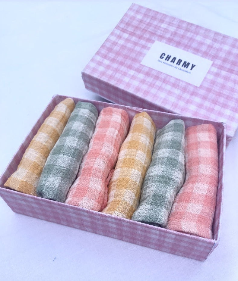coffret type boîte de 6serviettes de table en tissu. Elles sont roulées dans la boîte, il y a 2 serviettes vichy vert de gris, 2 rose barbapapa et 2 jaune blé