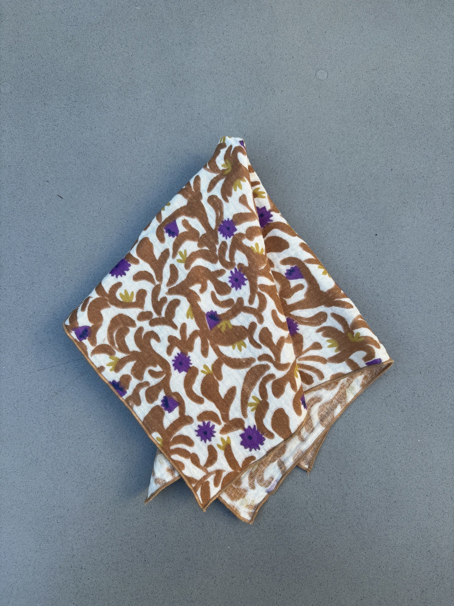 Serviette de table Nahili pliée, feuillage caramel et fleurs violettes sur double gaze de coton