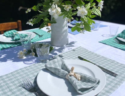 Serviette de table en tissu vichy vert de gris posée sur une assiette blanche